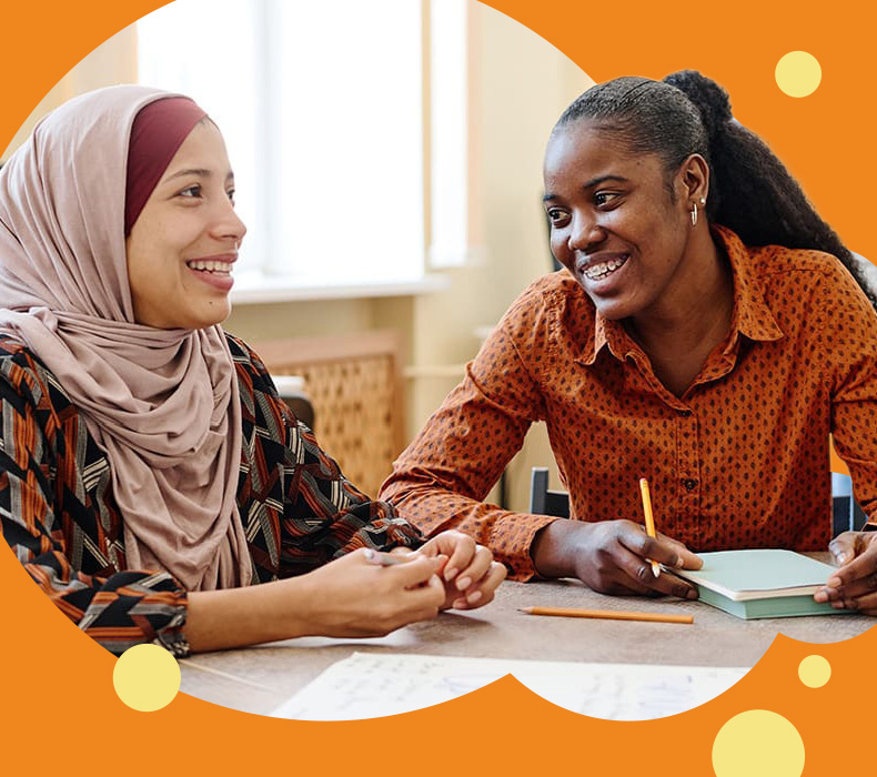 Two young women working together, one of whom is wearing a headscarf
